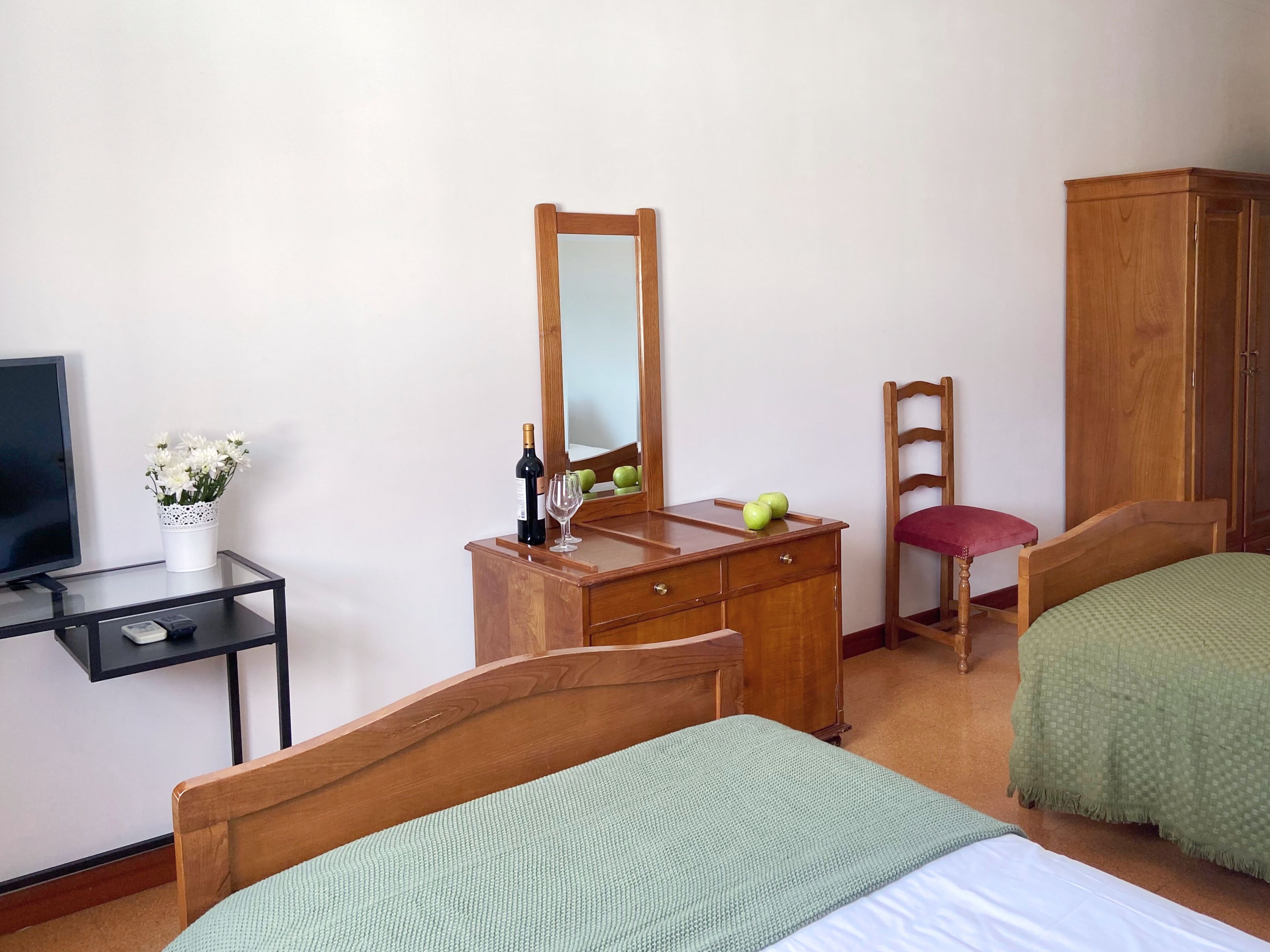 A bedroom with two beds, a wooden dresser, a mirror, a television, and a small table with a vase of flowers.