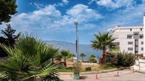 A street with palm trees, a street lamp, and a building with a view of the sea. - Franklin Rooms (Sarandë)