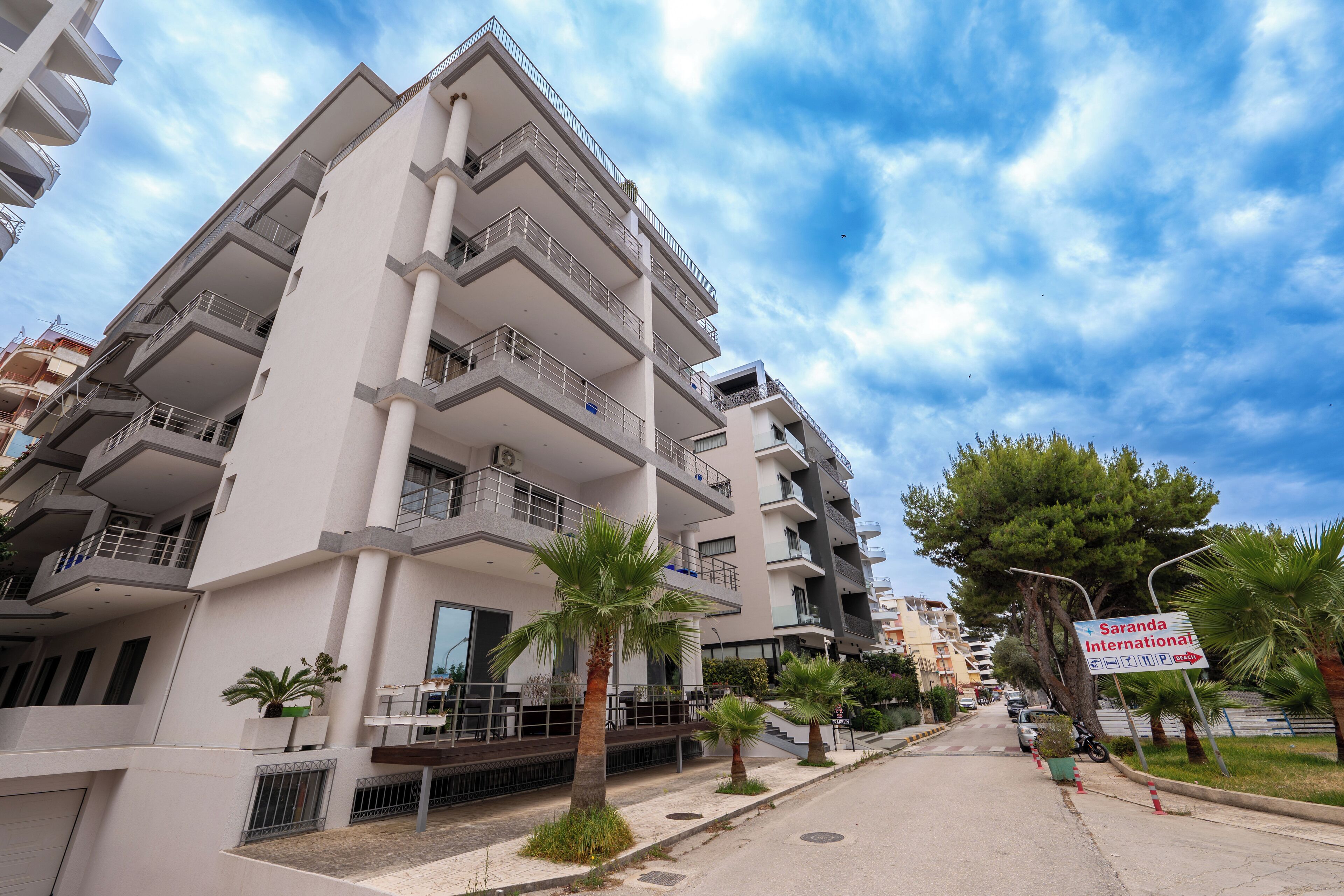 Un immeuble résidentiel à plusieurs étages, doté de balcons, donnant sur la rue et portant une enseigne indiquant « Sardana International ».