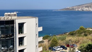 A modern building with multiple balconies overlooking a coastal area with parked cars and a view of the sea. - Franklin Rooms (Sarandë)
