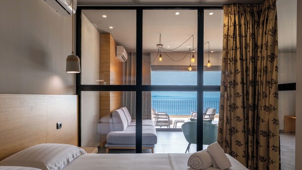 A hotel room with a large bed, a balcony with seating, and a view of the sea. - Franklin Rooms (Sarandë)