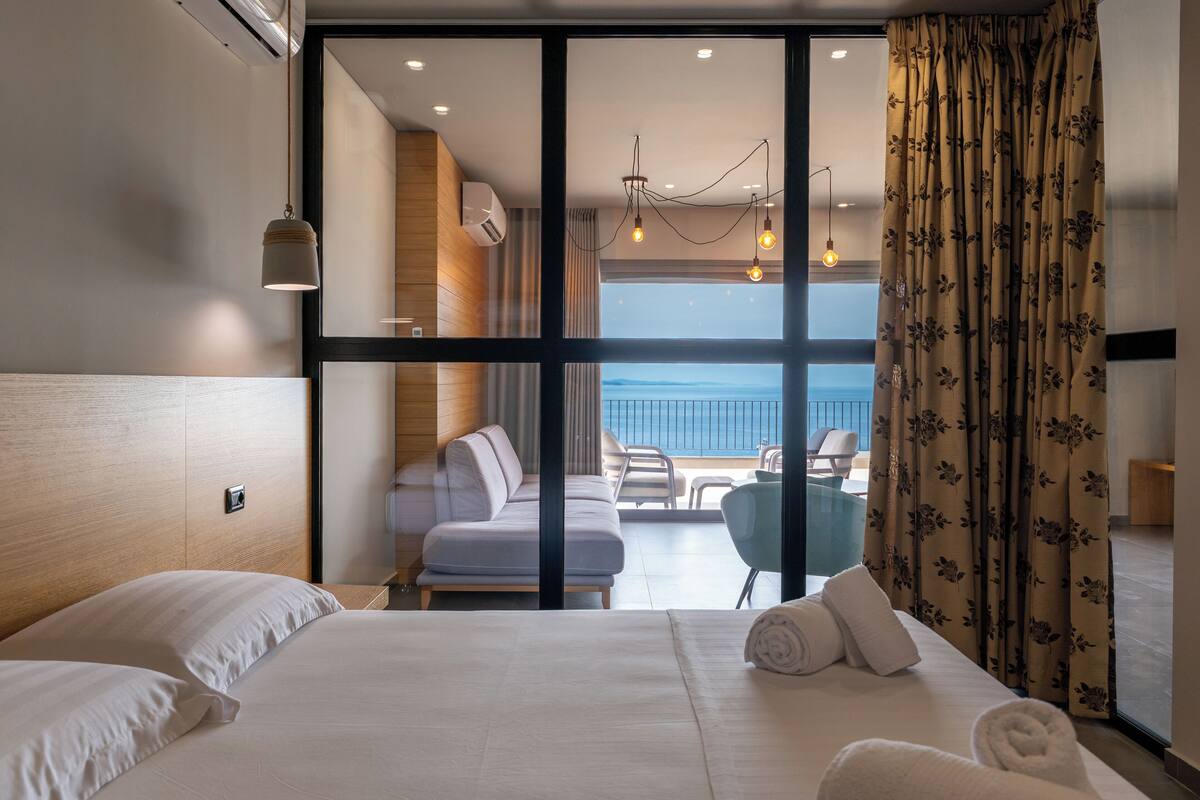 A hotel room with a large bed, a balcony with seating, and a view of the sea.
