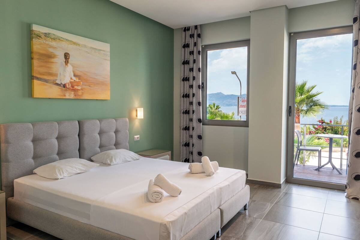 A double bed with white linens, a headboard, and two rolled towels on the bed.
