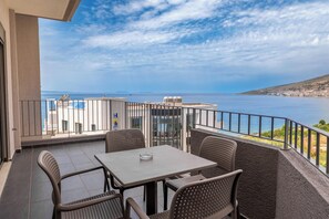 A balcony with a table and chairs, overlooking a coastal view with buildings and the sea. - Franklin Rooms (Sarandë)