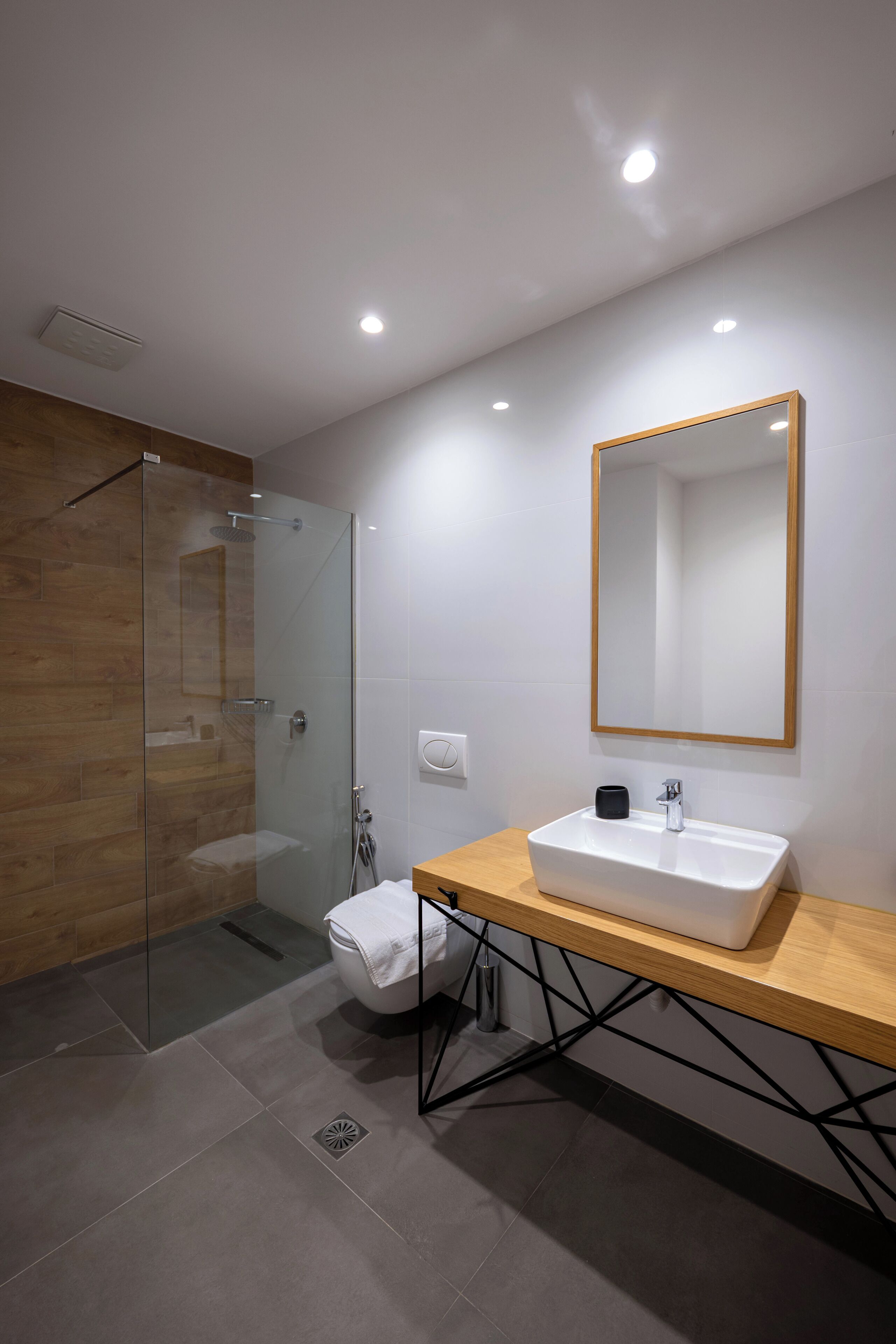 Une salle de bain moderne avec une douche à parois de verre, un lavabo blanc doté d’un plan de toilette en bois et un grand miroir mural.
