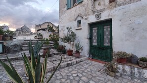 A courtyard with stone steps leading to a building with a green door. There are potted plants and a statue on the steps. - 1 Bedroom Guesthouse in Matera (Matera)