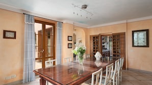 A dining area with a wooden table, white chairs, a vase with flowers, and a kitchen in the background. - Villa Monte Bottigli (Grosseto)
