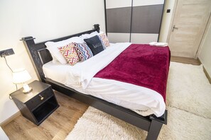 A neatly made bed with patterned pillows, a white comforter, and a red throw blanket. - Lavington View Palace Apartment (Nairobi)