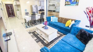A modern living room with a blue sofa, a coffee table, and a dining area with chairs and a table. - Lavington View Palace Apartment (Nairobi)
