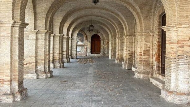 Un couloir voûté, orné de colonnes en pierre et doté d’un sol carrelé, qui mène à une porte au fond.