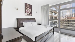A modern hotel room with a large bed, a nightstand, a painting on the wall, and a view of the city through large windows. - WelHome - Urban Retreat With Terrace And City Views (Dubai)