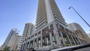 A tall, modern building with multiple floors and balconies, surrounded by other high-rise buildings. - WelHome - Urban Retreat With Terrace And City Views (Dubai)