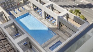 An aerial view of a rooftop pool area with multiple lounge chairs and a swimming pool. - WelHome - Urban Retreat With Terrace And City Views (Dubai)