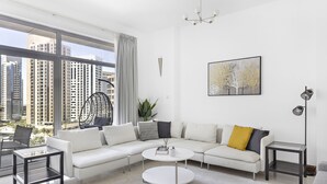 A modern living room with a white sectional sofa, a round coffee table, and a view of tall buildings through large windows. - WelHome - Urban Retreat With Terrace And City Views (Dubai)