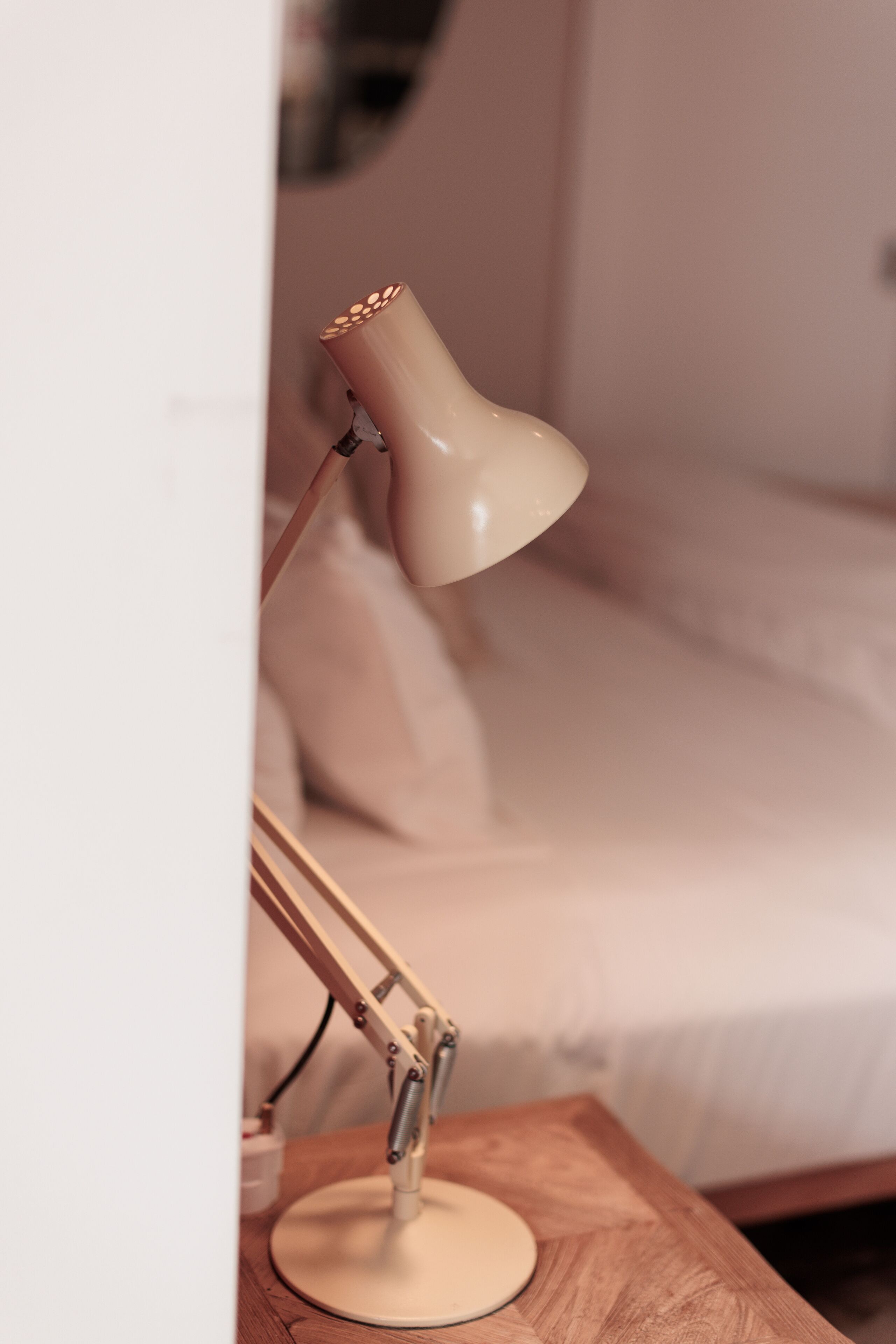 A bedside table with a lamp, a bed with a white cover, and a wooden nightstand.