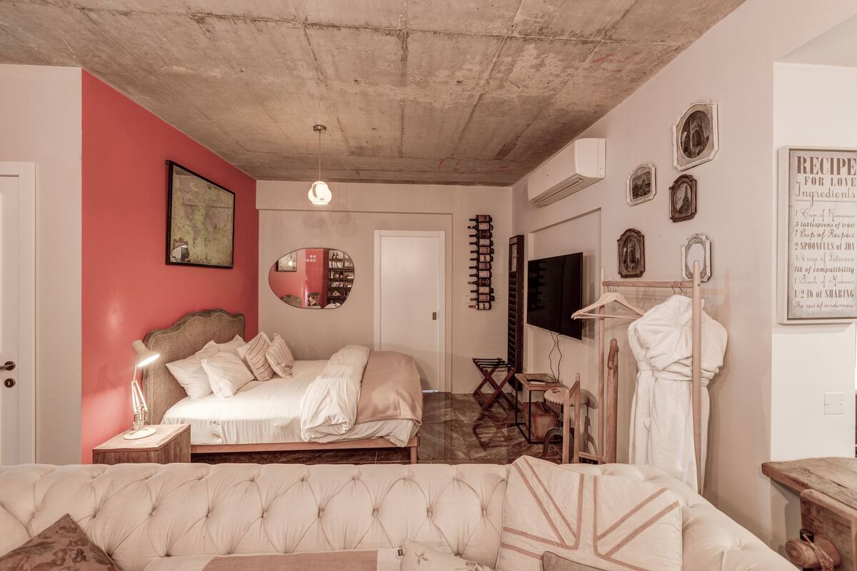 Ein Schlafzimmer mit Bett, einer Couch, einem Kleiderschrank, einem Fernseher und einer Wand mit gerahmten Bildern und einem Rezeptplakat.