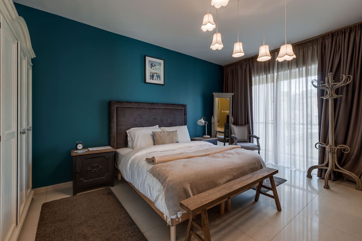 Ein Schlafzimmer mit Bett, Nachttischen, einer Bank, einem Kleiderschrank und einem Spiegel.