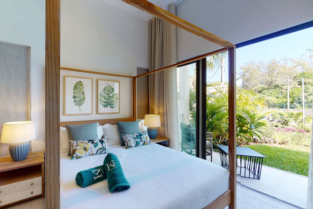 Habitación de hotel moderna con una cama grande, dos mesitas de noche con lámparas, vistas a un jardín a través de ventanas de techo a suelo y obras de arte en las paredes.