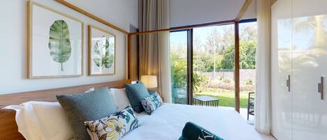 A hotel room with a large bed, a view of the garden, and framed artwork on the wall.