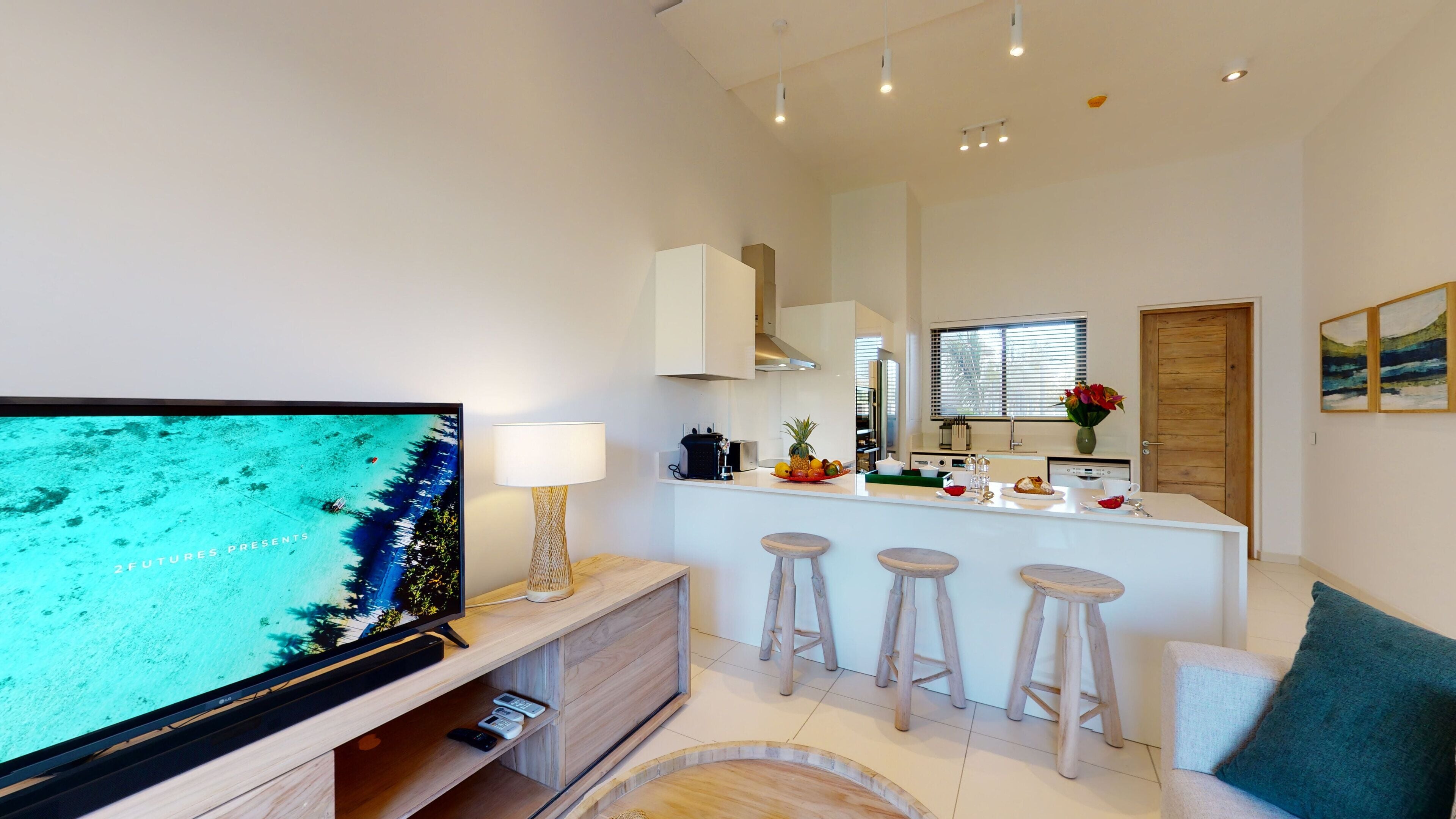 A modern kitchen with a central island, bar stools, a TV, and a dining area with a sofa.