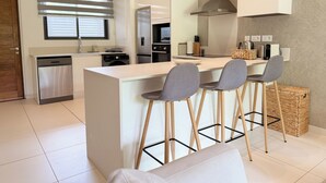 A modern kitchen with a central island, bar stools, and a built-in stove. -  Ki Residences with LOV (Grand-Baie)