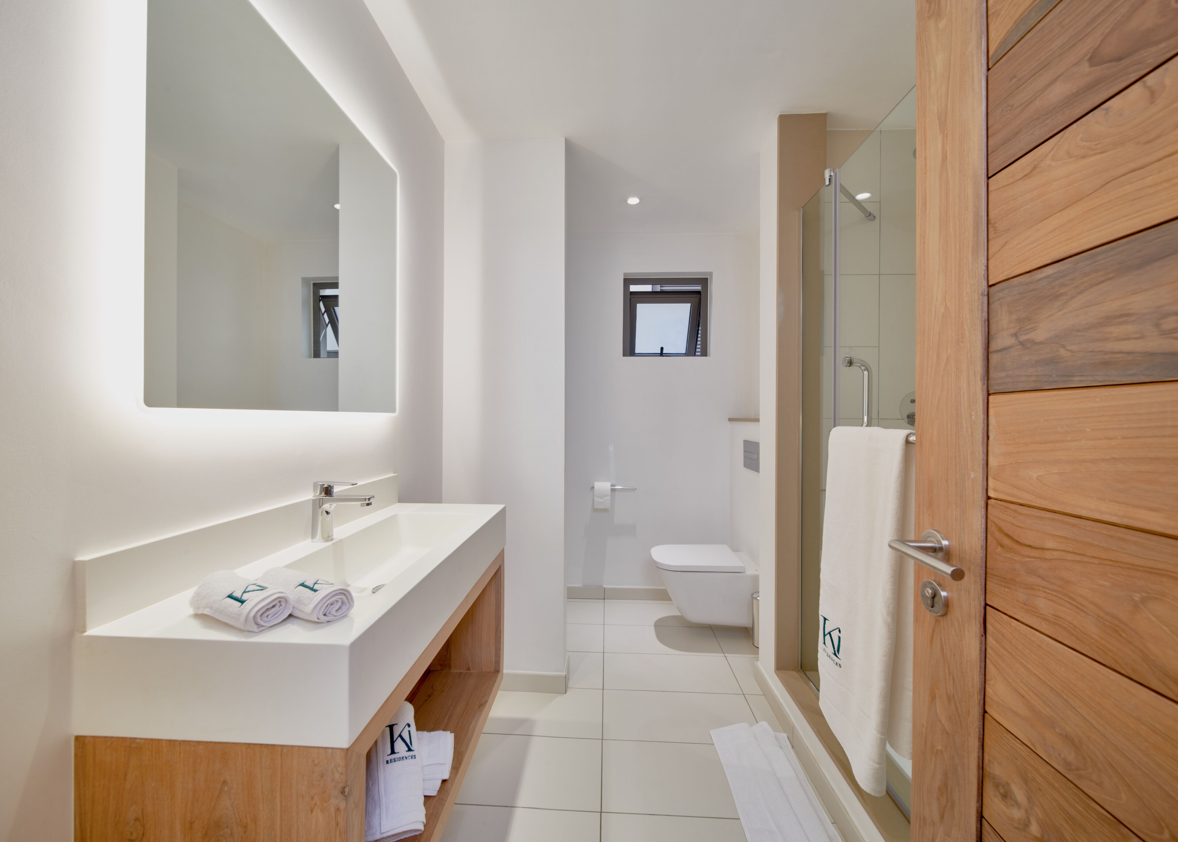 A modern bathroom with a white vanity, a large mirror, a glass shower enclosure, and a wooden door.