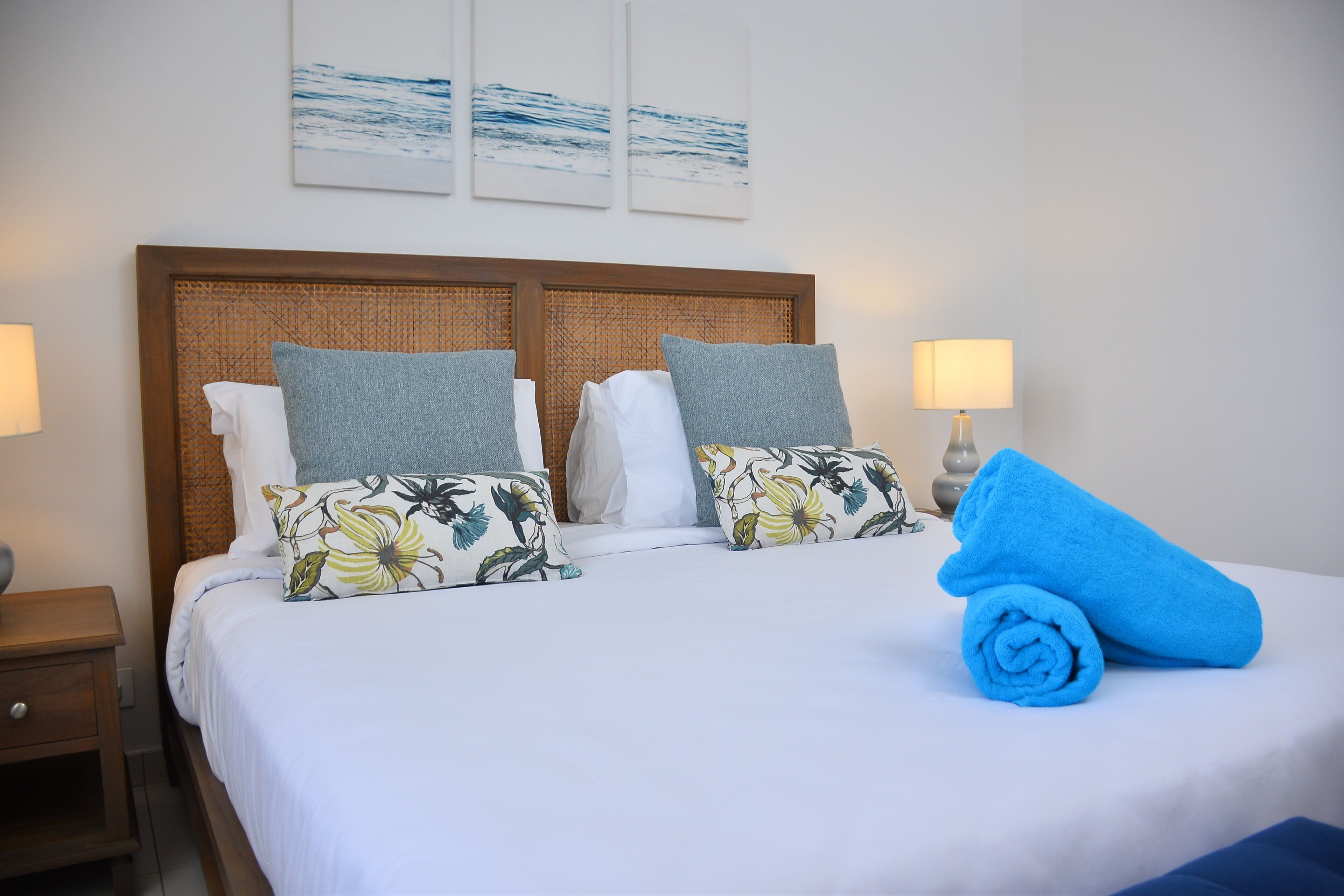 Una cama bien hecha con almohadones florales, una toalla azul y un cabecero de madera.