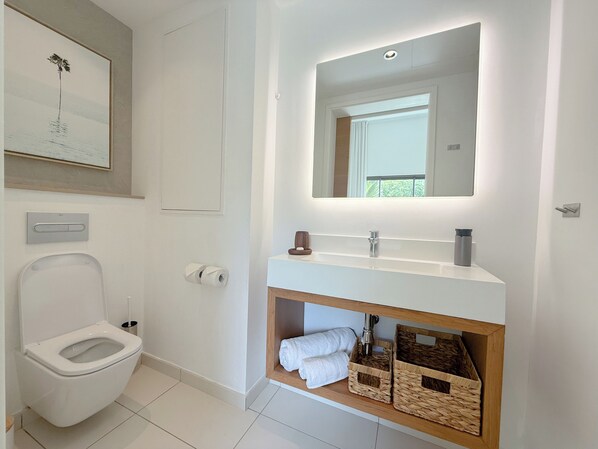 A modern bathroom with a toilet, a sink with a mirror, and a shower.