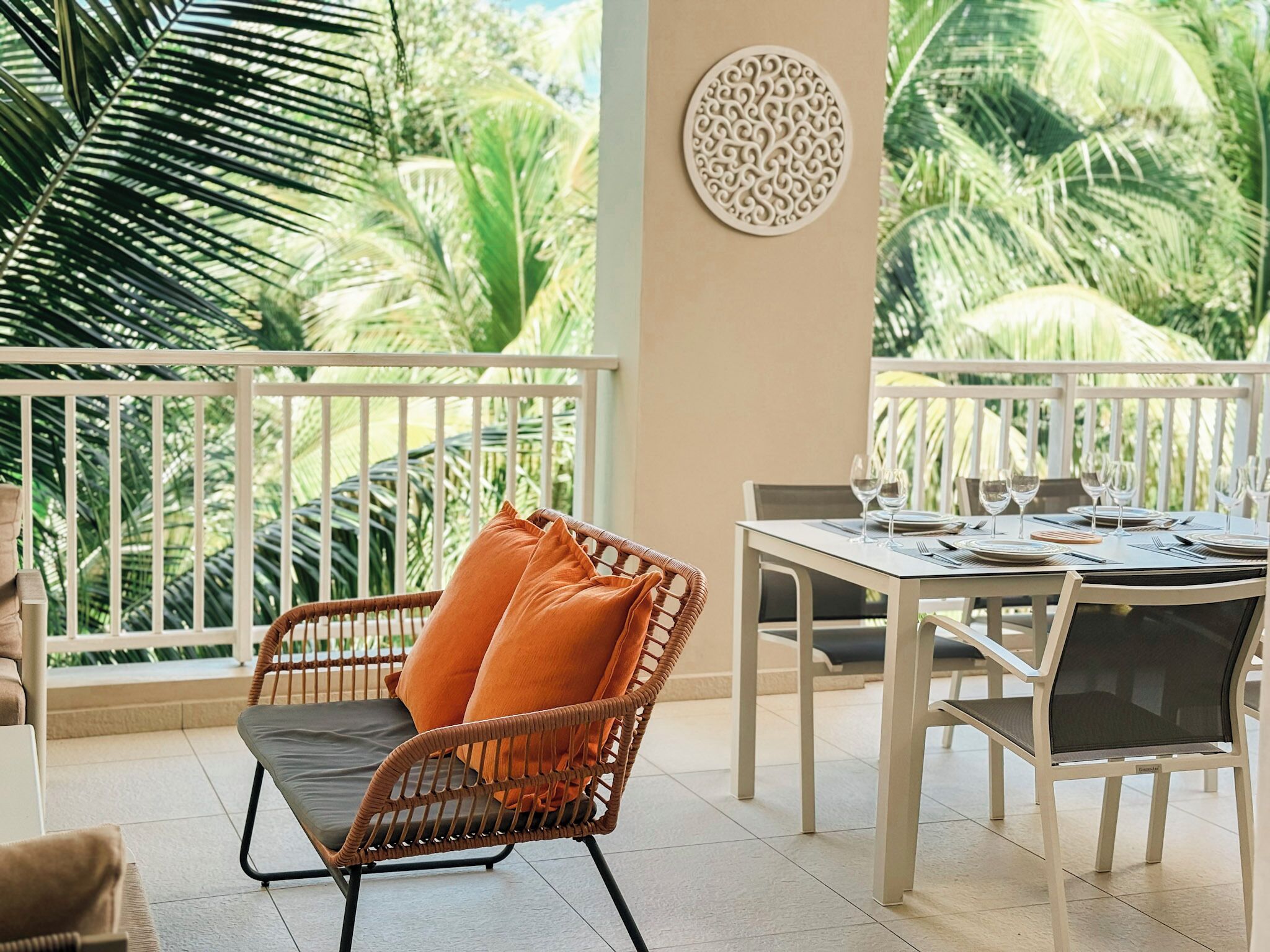 Un balcone con una sedia in vimini, un tavolo da pranzo apparecchiato con piatti, bicchieri e posate.