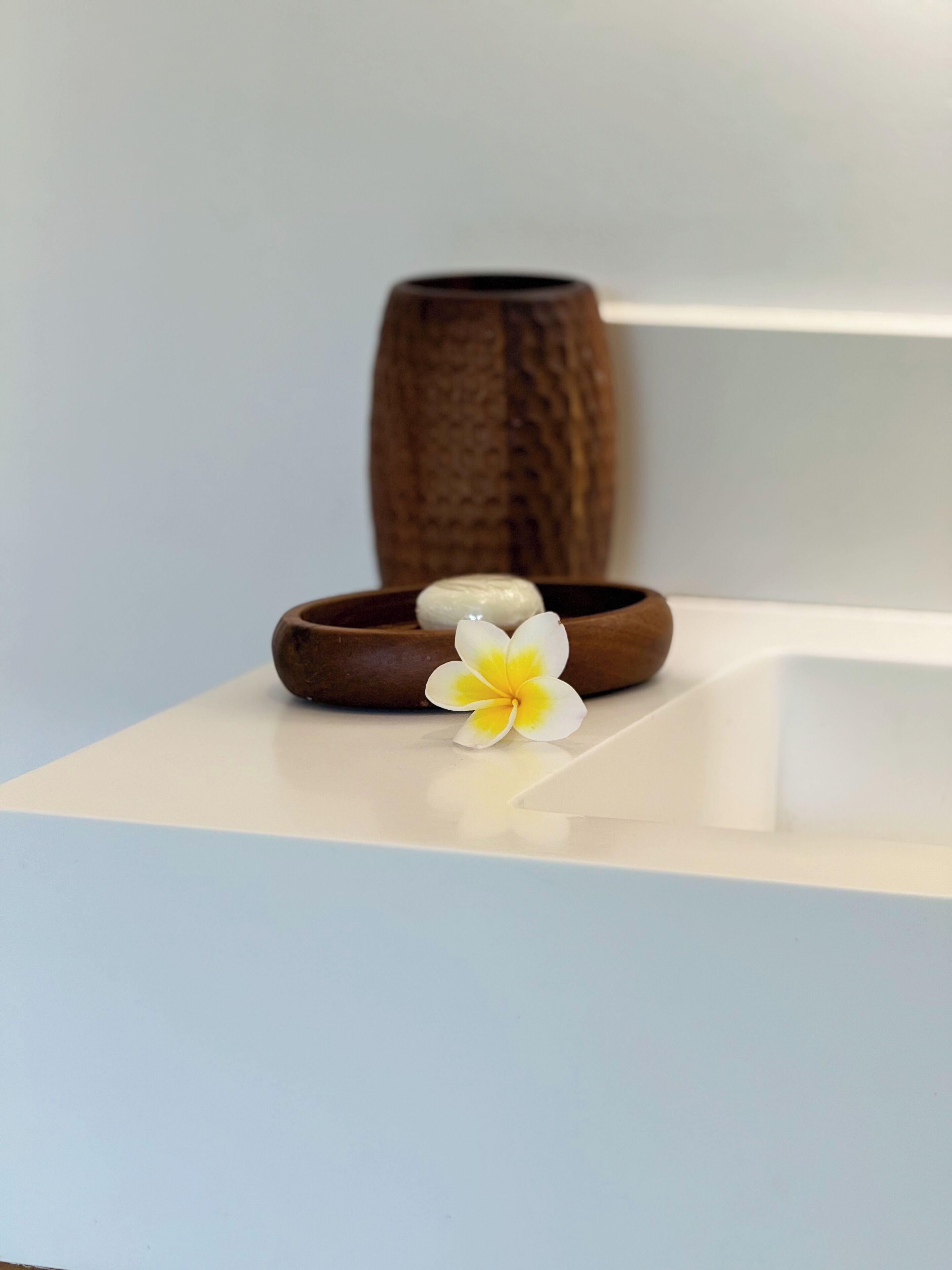 A wooden bowl with a stone and a yellow flower on a white surface.