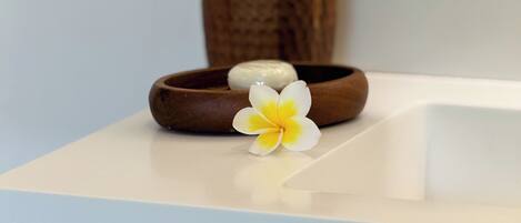 A wooden bowl with a stone and a yellow flower on a white surface.