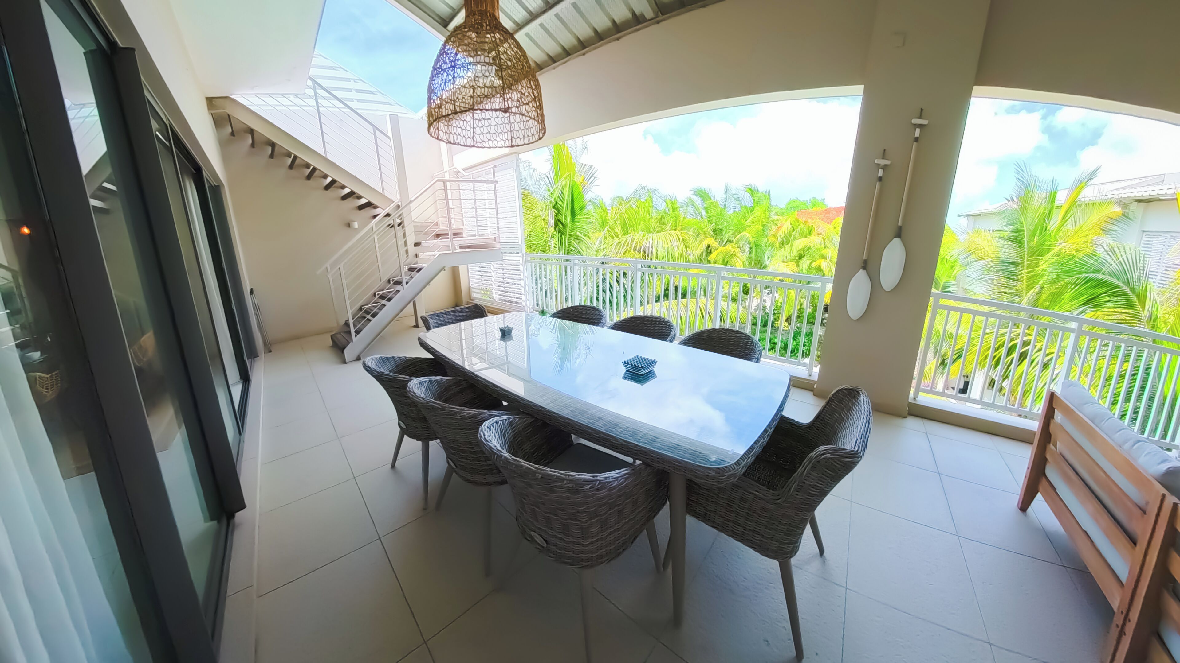 Ein Balkon mit Esstisch und Stühlen, eine Treppe und Blick auf üppiges Grün.