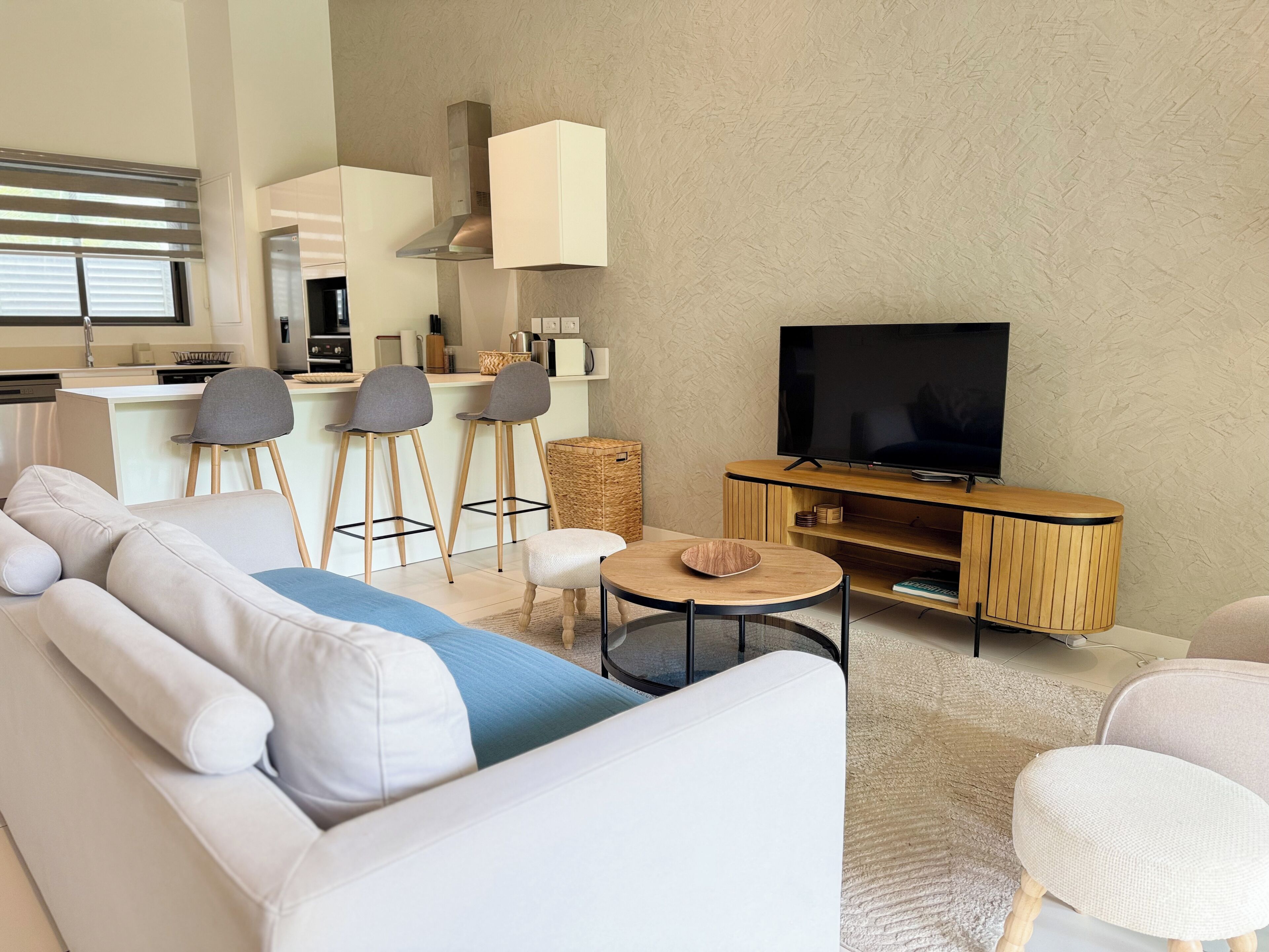 A modern living room with a sofa, chairs, a coffee table, a TV, and a kitchen area.