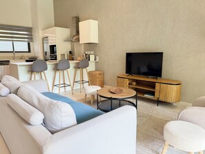 Uma sala de estar moderna com sofá, cadeiras, mesa de centro, televis ão e área de cozinha.