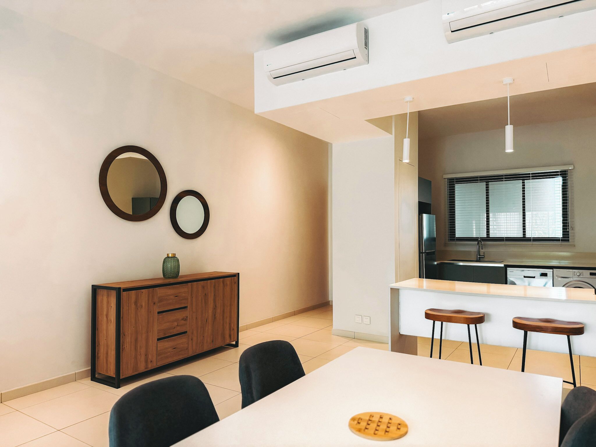 A modern kitchen with a built-in dishwasher, a dining area with a table and chairs, and a large window with blinds.
