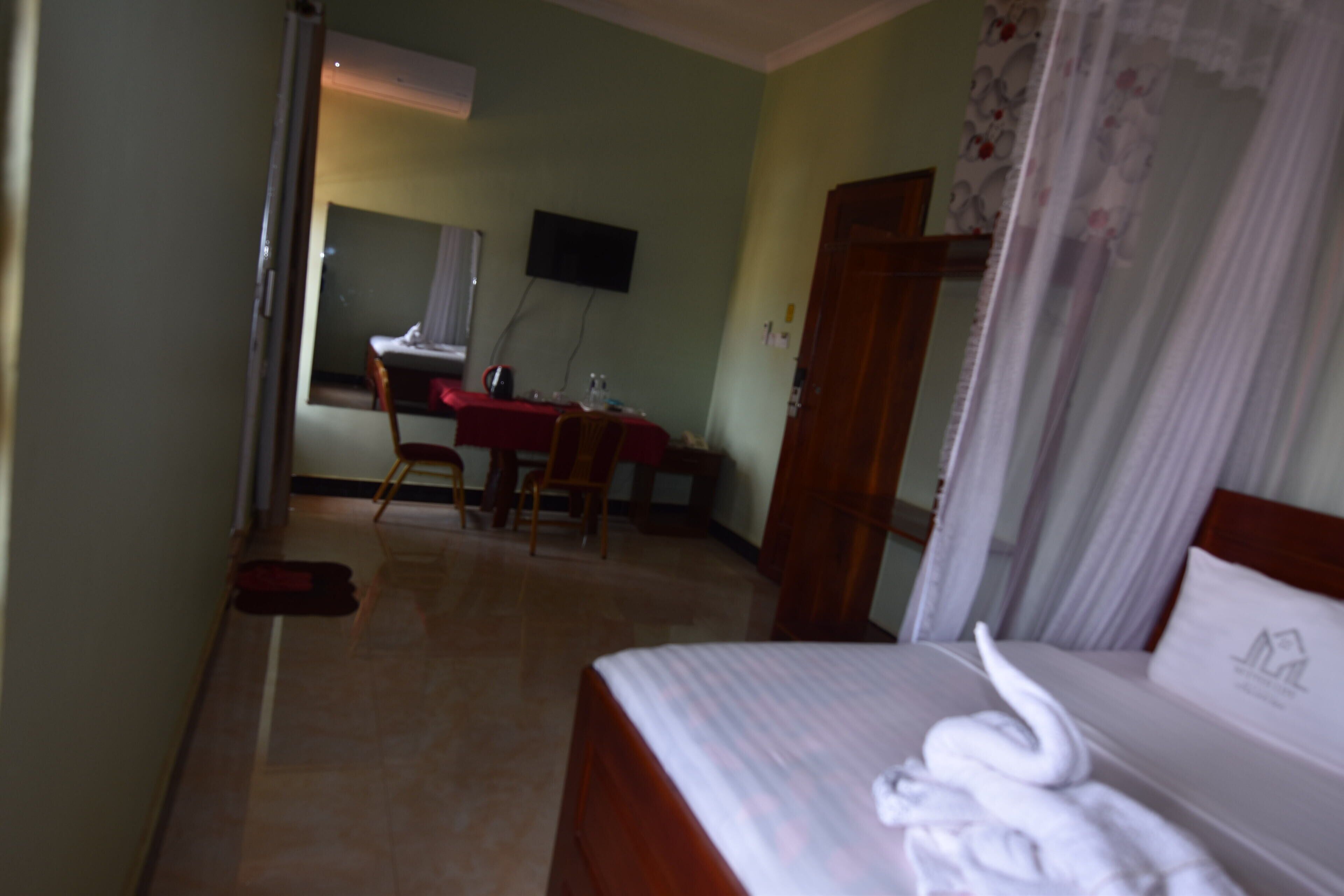 A hotel room with a bed, a desk with a chair, a television on the wall, and a door with a curtain.