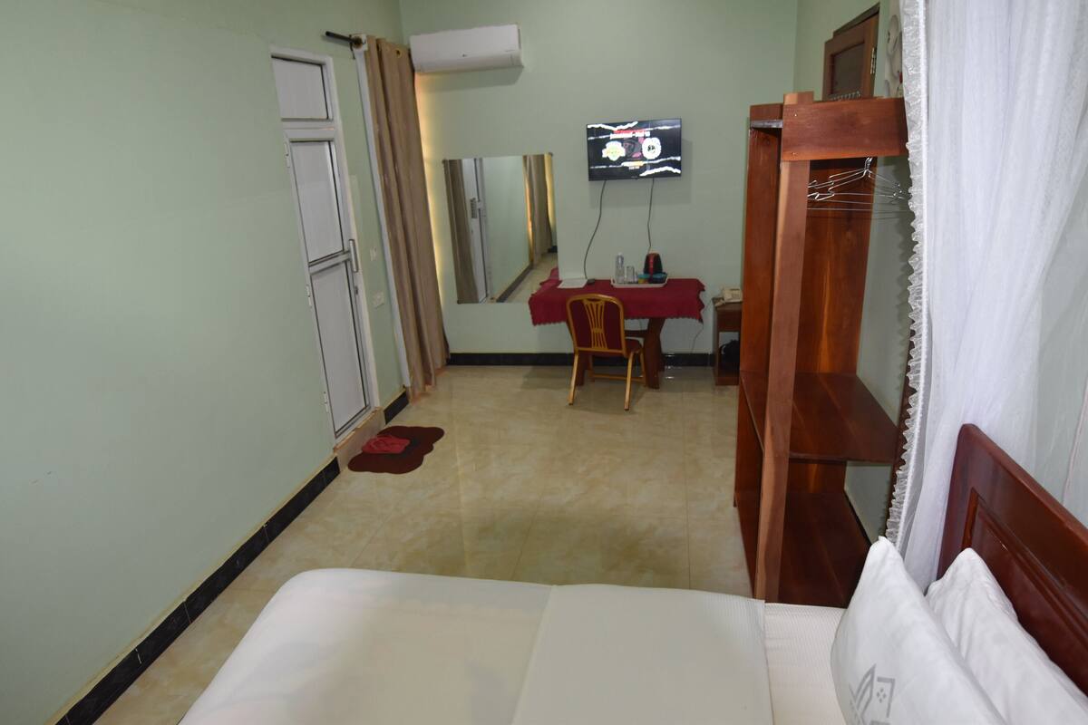 Ein Hotelzimmer mit einem Bett, einem Schreibtisch mit Stuhl, einem Fernseher und einem Kleiderschrank.