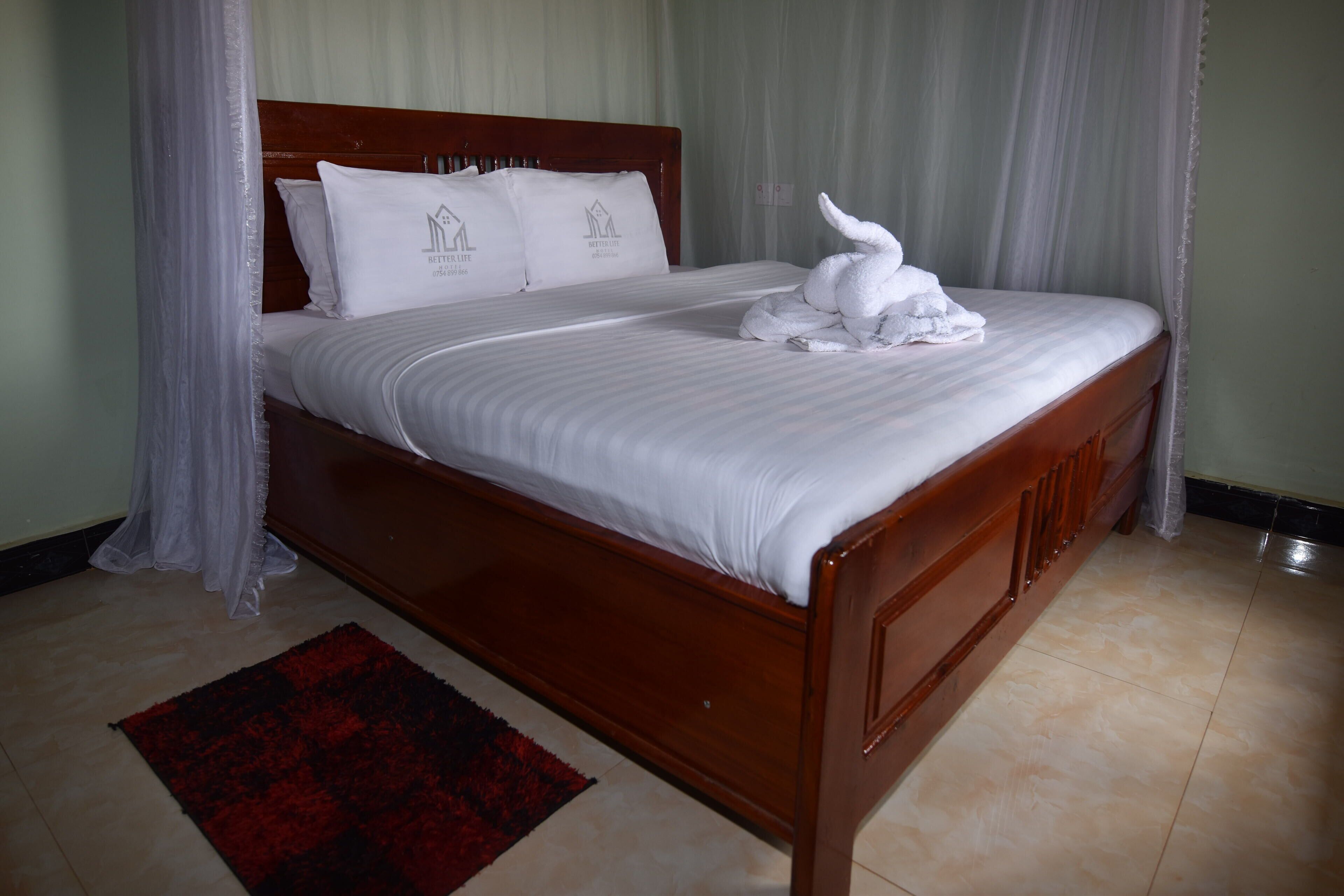 A neatly made bed with white linens and pillows, a wooden headboard, and a red and black patterned rug on the floor.