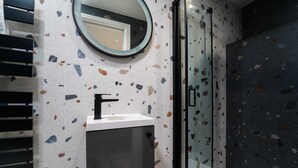 A modern bathroom with a glass shower enclosure, a freestanding sink with a white countertop, and a circular mirror above the sink.