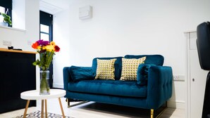 A modern living room with a teal sofa, patterned cushions, a small white side table, and a patterned rug.