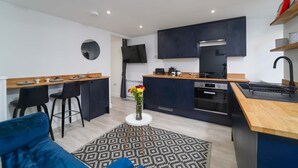 A modern kitchen with dark cabinets, a wooden countertop, and a built-in oven. There is a round table with a vase of flowers in the center of the room.