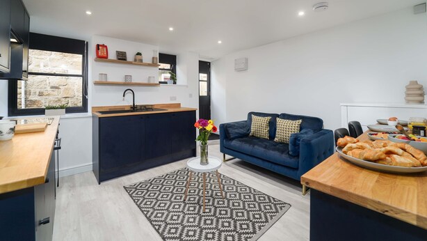 A modern kitchen with a central island, a dining area with a blue sofa, and a small side table with pastries.