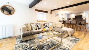 A modern living room with a sofa, coffee table, and a kitchen area in the background. - The Boathouse, St Ives – Sleeps 4 – Dog-Friendly (St Ives)