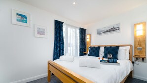 A neatly arranged bedroom with a wooden bed, white linens, and a bedside table with a kettle and cups. - Little Waves, St Ives – Sleeps 2 – Courtyard - Garage Parking (St Ives)