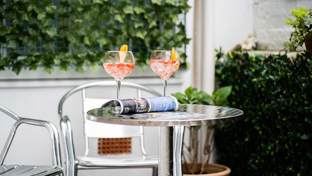 Two drinks on a table with a magazine, surrounded by greenery. - Little Waves, St Ives – Sleeps 2 – Courtyard - Garage Parking (St Ives)