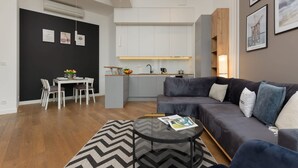 Una sala de estar moderna con un sofá seccional gris, una mesa de centro redonda de vidrio y un comedor con mesa y sillas blancas.
