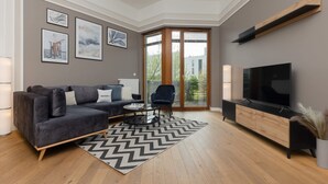 Una sala de estar moderna con un sofá gris oscuro, un tapete a cuadros blanco y negro, un mueble de madera con un televisor y un ventanal con vistas a zonas verdes.
