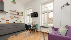 Una cocina moderna con armarios de madera, un área de comedor con sillas, un sofá púrpura y un televisor montado en la pared.