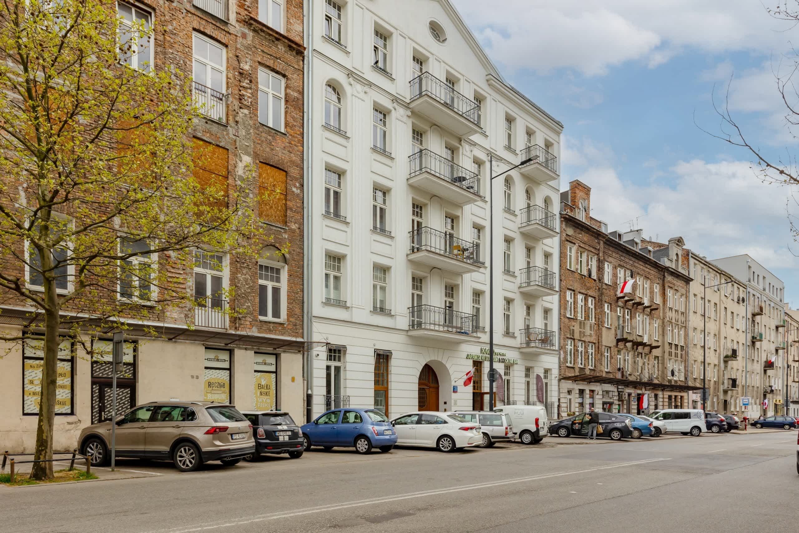 Una fila di edifici a più piani con diversi stili architettonici, tra cui facciate in mattoni e bianche, lungo una strada con auto parcheggiate.