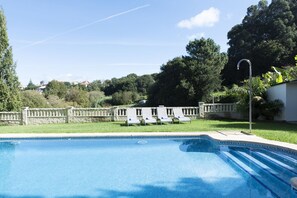 Una piscina con pared de piedra y sillas de descanso.